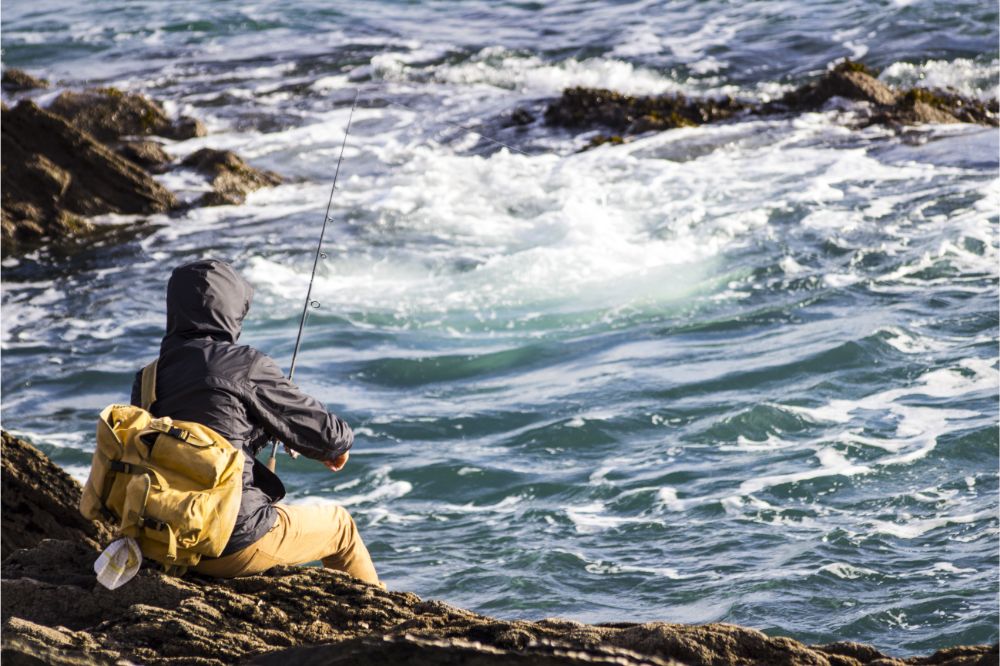 Man with backpack sitting on rocks fishing