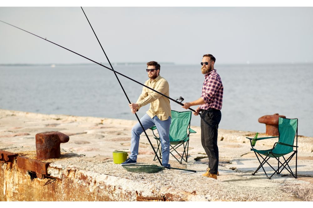 happy friends with fishing rods on pier at sea