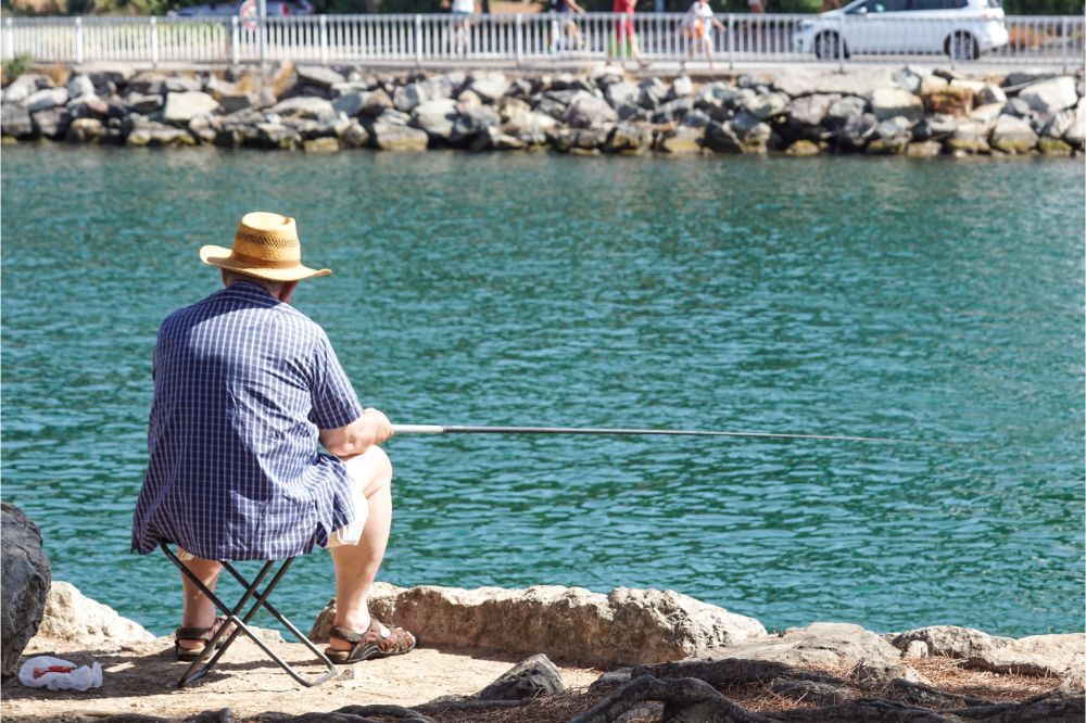Retired senior man enjoys fishing from a pier into the river