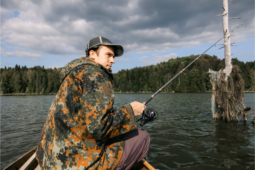 A guy in a jacket and a cap with a fishing rod in his hands