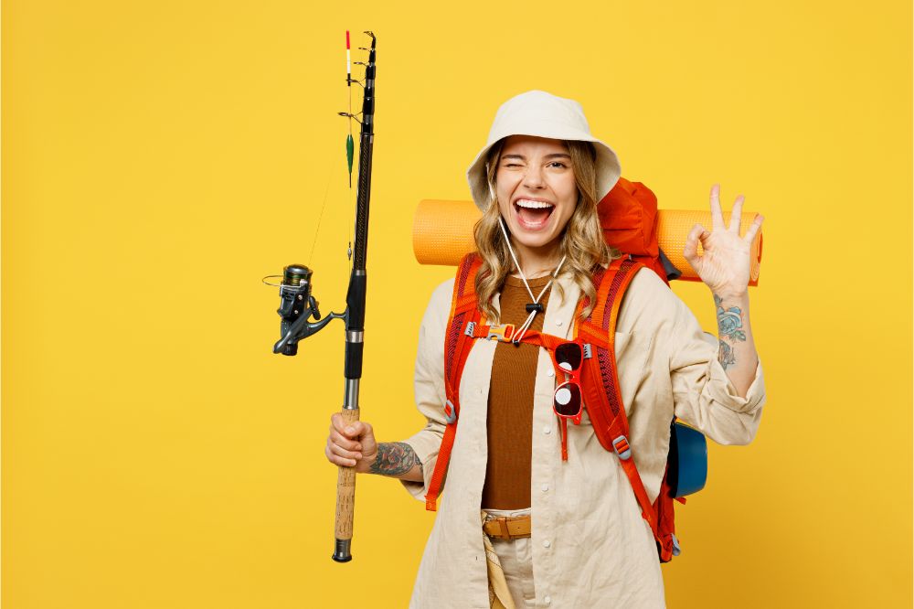 Young fun woman carry backpack with stuff mat hold fishing rod